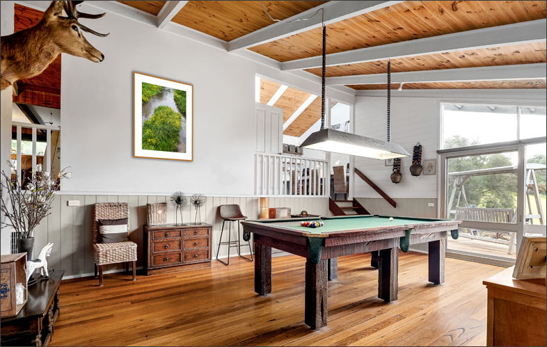 Salon lumineux avec billard et plafond en bois, d�cor� d�une photo encadr�e repr�sentant le lit de l�Orne bord� d�une v�g�tation verdoyante o� s��panouissent des fleurs jaunes.