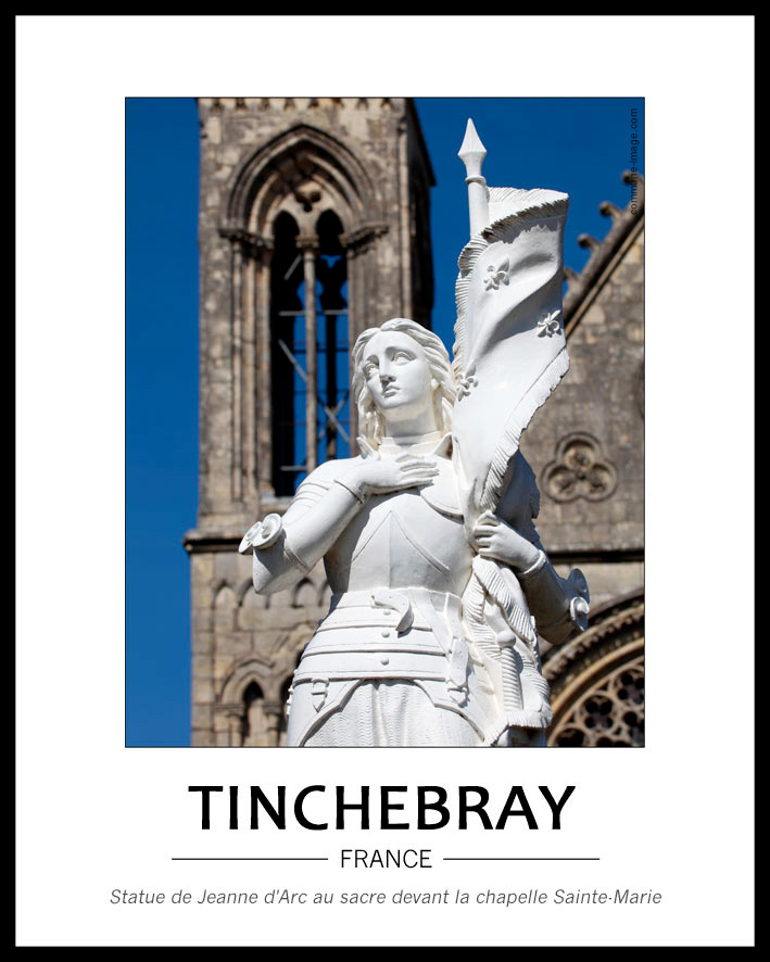 Cliquez pour agrandir Au centre de la petite place située devant la chapelle Sainte-Marie se tient la statue de Jeanne d'Arc, de couleur blanche. On voit le haut de son corps à partir de sa taille, elle est en armure, porte un étendard. Au fond on voit floue une des tours
