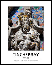 vue tr�s rapproch�e de la vierge � l'enfant devant la rosace. On voit juste le buste de la vierge et l'enfant dans son int�gralit�, les bras �cart�s. la pierre grise de l'�difice est raviv�e par les couleurs marqu�es des vitraux de la rosace.